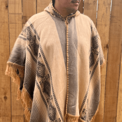 Gold poncho with South American pattern on model standing in front of a fence