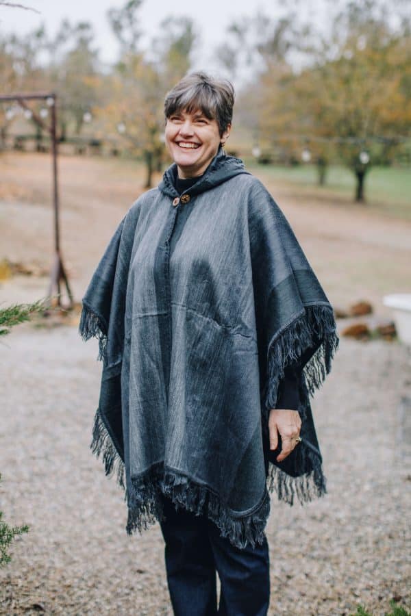 Smiling model outdoors wearing charcoal gray poncho with fringed edge and hood