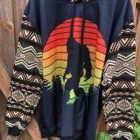 Black no-zip hoodie with image of Bigfoot silhoutted against a sunset. Sleeves are native pattern.