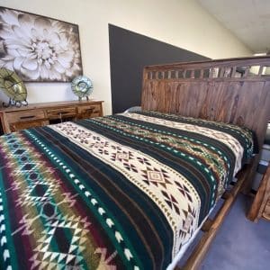 Southwestern pattern green and raspberry blanket on bed in bedroom showroom.