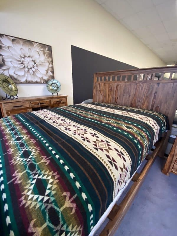 Southwestern green blanket with raspberry colored accents on bed in bedroom showroom.