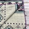 Southwestern design blanket in purple and turquoise folded open to show cream colored reverse side.