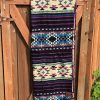 Southwestern pattern blanket in purple, turquoise and cream, folded and atop a wooden gate.