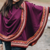 Model wearing wine-colored capelet with shoulder button and rounded shape.
