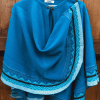 Tropical Blue capelet with rounded silhouette and shoulder button, hanging on wooden fence