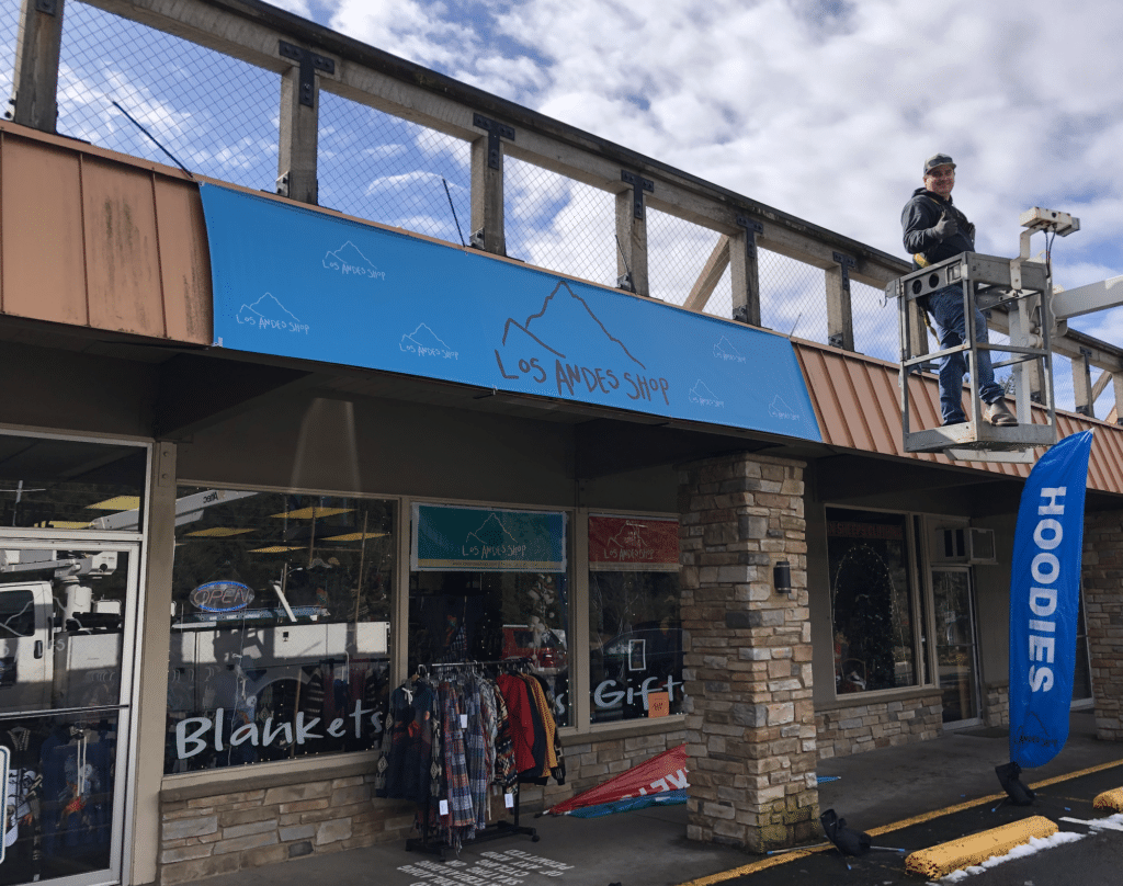 Man on cherry picker installing sign above Los Andes Shop 68212 E Hwy 26 Welches OR