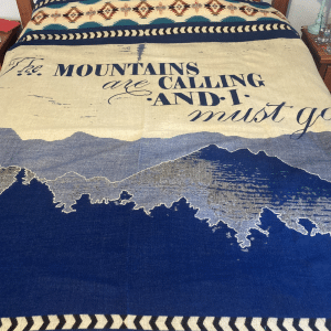 Blue and white blanket with image of mountains and trees and words The mountains are calling and I must go.