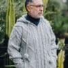 Male model wearing handknit light gray 100% wool zip hoodie, standing in front of large cacti.