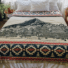 Cream colored blanket with mountain image and geometric border, displayed on bed