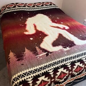 Blanket on bed shows Sasquatch figure in cream on dark red and orange background