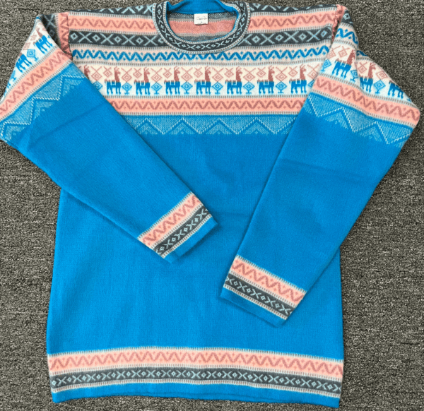 Sky blue crewneck sweater with pink black and cream design on yoke featuring llamas, laying flat on a gray surface