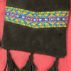 Small square black suede crossbody purses with woven yellow band, one has 3 tassels, one has no tassels, laying against a red background