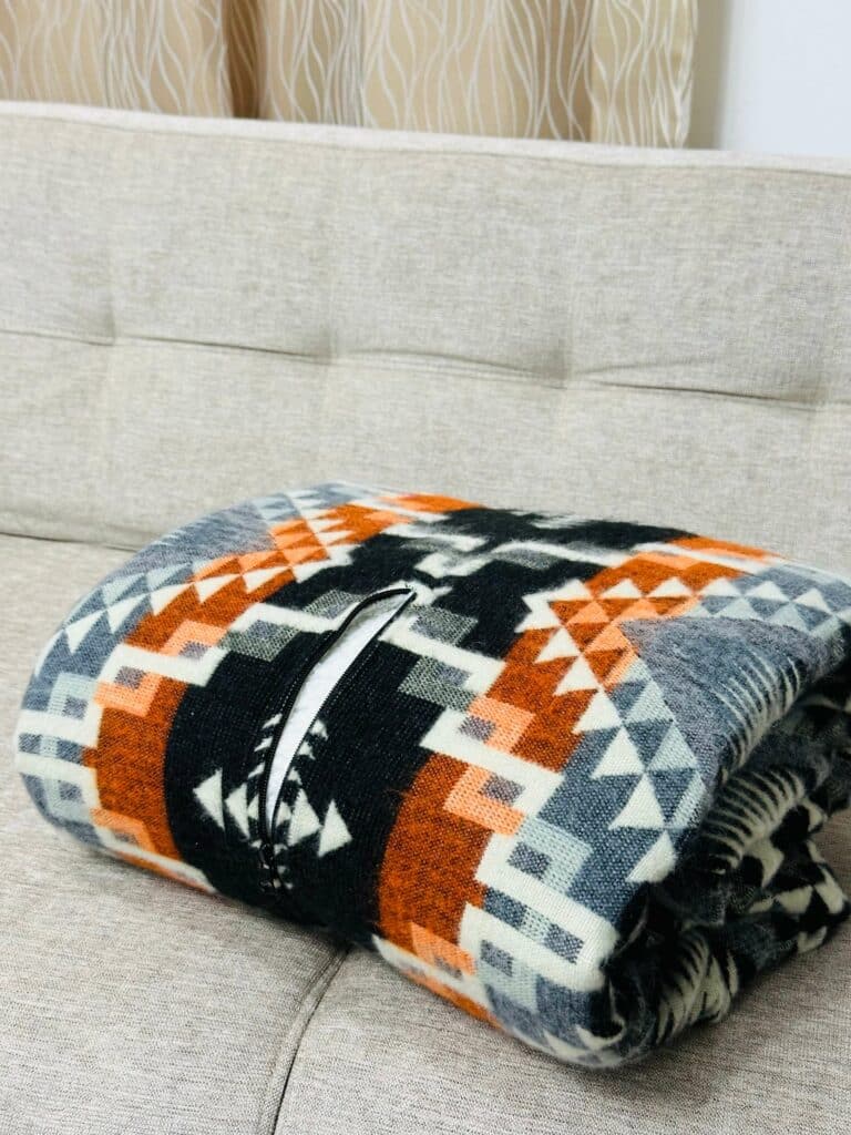 Orange, black and grey blanket poncho folded on couch