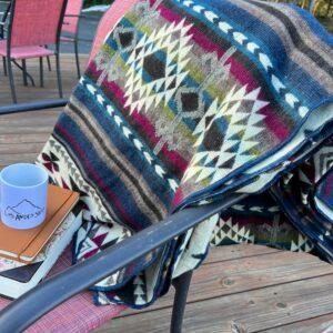 Jewel Tone Blanket with Southwestern design across back of deck chair, with journal and coffee cup.