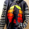Black hoodie with kangaroo pockets and geometric black and white sleeves, featuring Bigfoot figure making Rock On gesture against an orange and yellow sunset background
